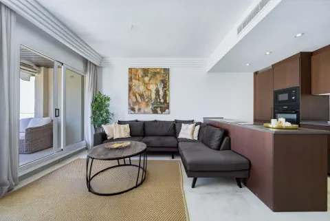 An open living room and kitchen with a grey corner sofa and dark wood units