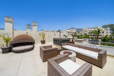 A roof terrace in the sun with a round day bed, wicker sofas and a fire table