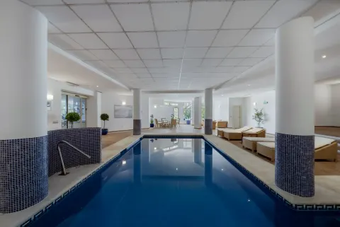 An indoor pool between tiled columns, loungers along one side