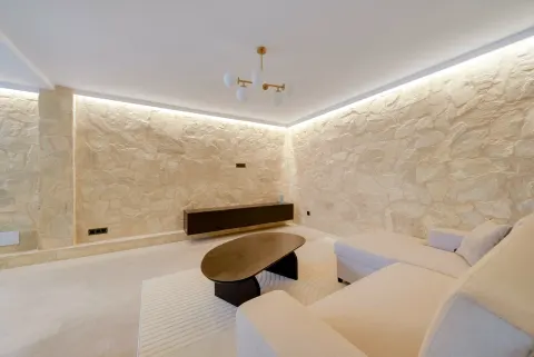 A living room with a lit stone wall, a low dark table and a pale sofa